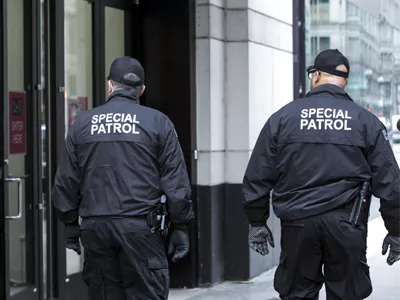 Two security personnel in black jackets labeled "SPECIAL PATROL" walking on a city street.